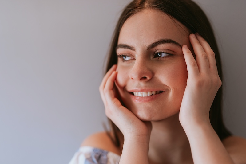 woman with clear skin smiling and touching her face